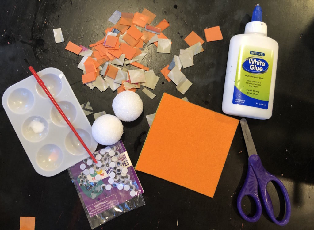 a tabletop of supplies: foam balls, glue, felt, tissue paper, googly eyes, and scissors