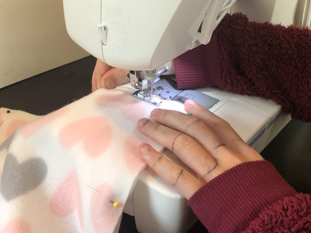 small hands work a sewing machine, seaming two pieces of fleece adorned with hearts