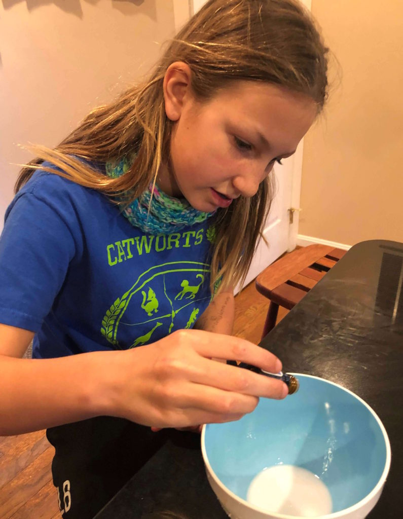 a young girl drips essential oils into a plastic bowl full of melted soap base