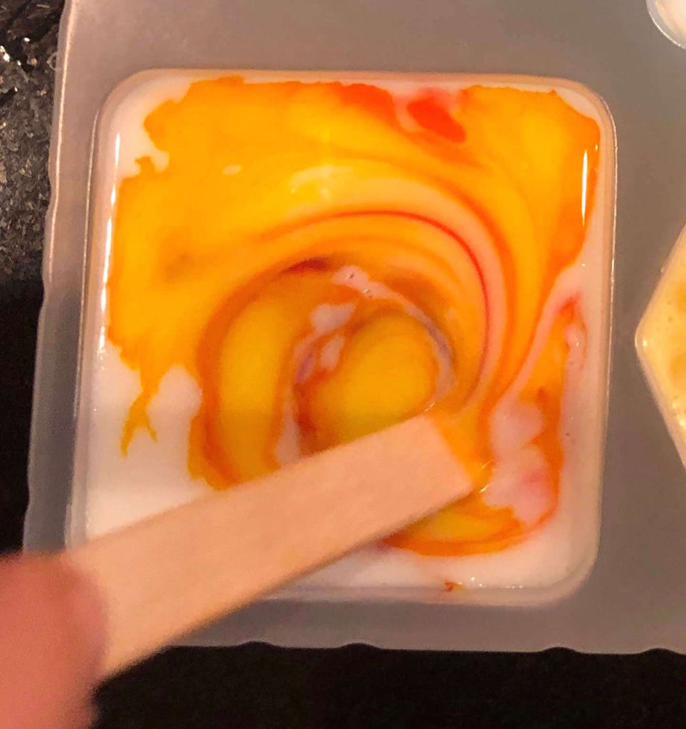 a Popsicle stick swirls a multicolor design into a setting bar of soap