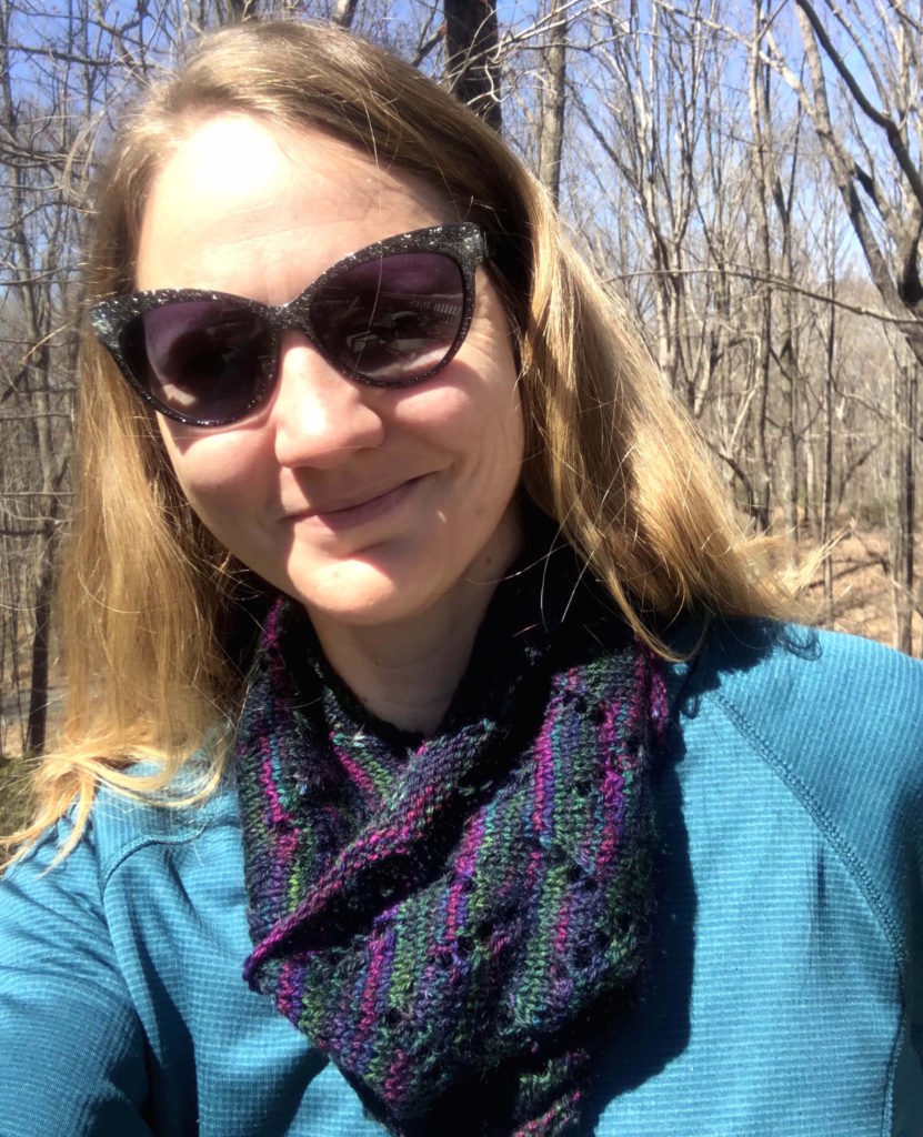 a woman wears a multicolored woolen cowl with v-shaped eyelets