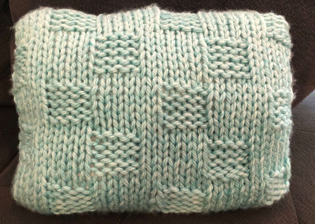 a light blue-green pillow with a basketweave stitch