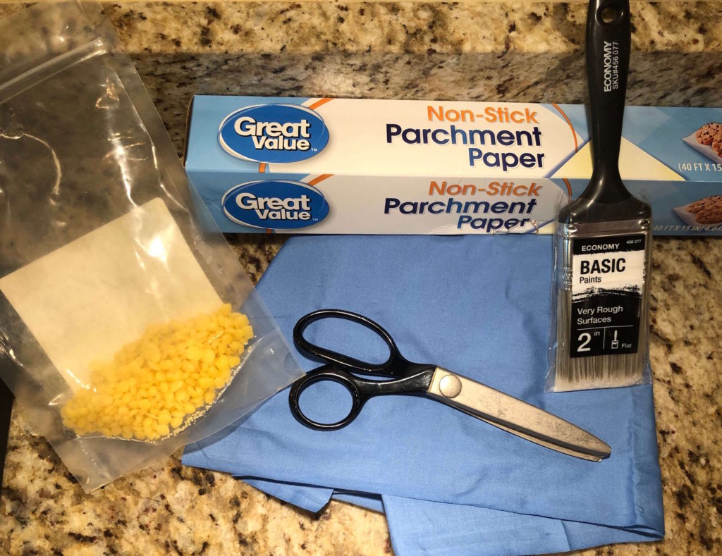 materials for making beeswax wrap: paint brush, scissors, cotton fabric, parchment paper, and beeswax pastilles