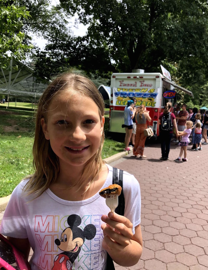 a young girl enjoys a fried Oreo outside the food truck where she bought it