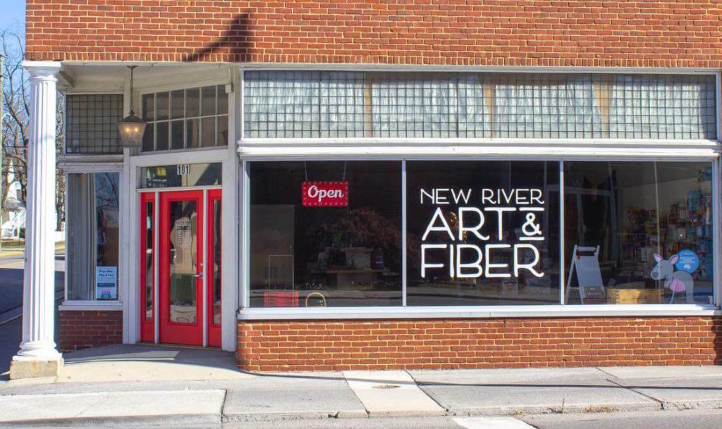 a brick and glass storefront reads "New River Art & Fiber/Open"