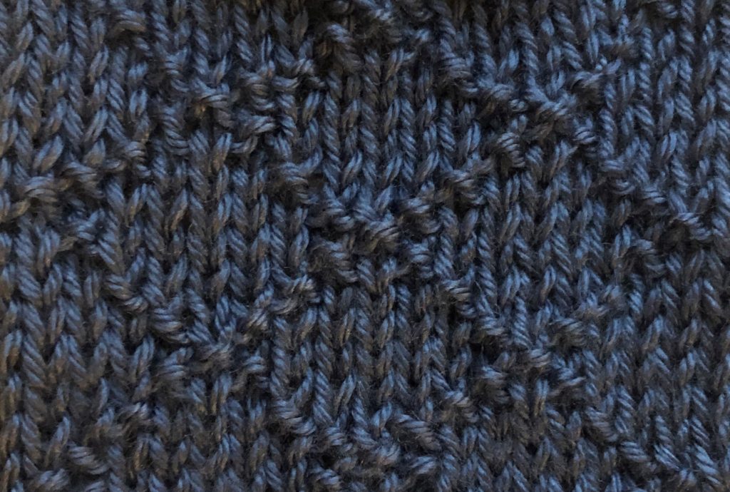 a close-up of diamond brocade stitch worked across blue fabric