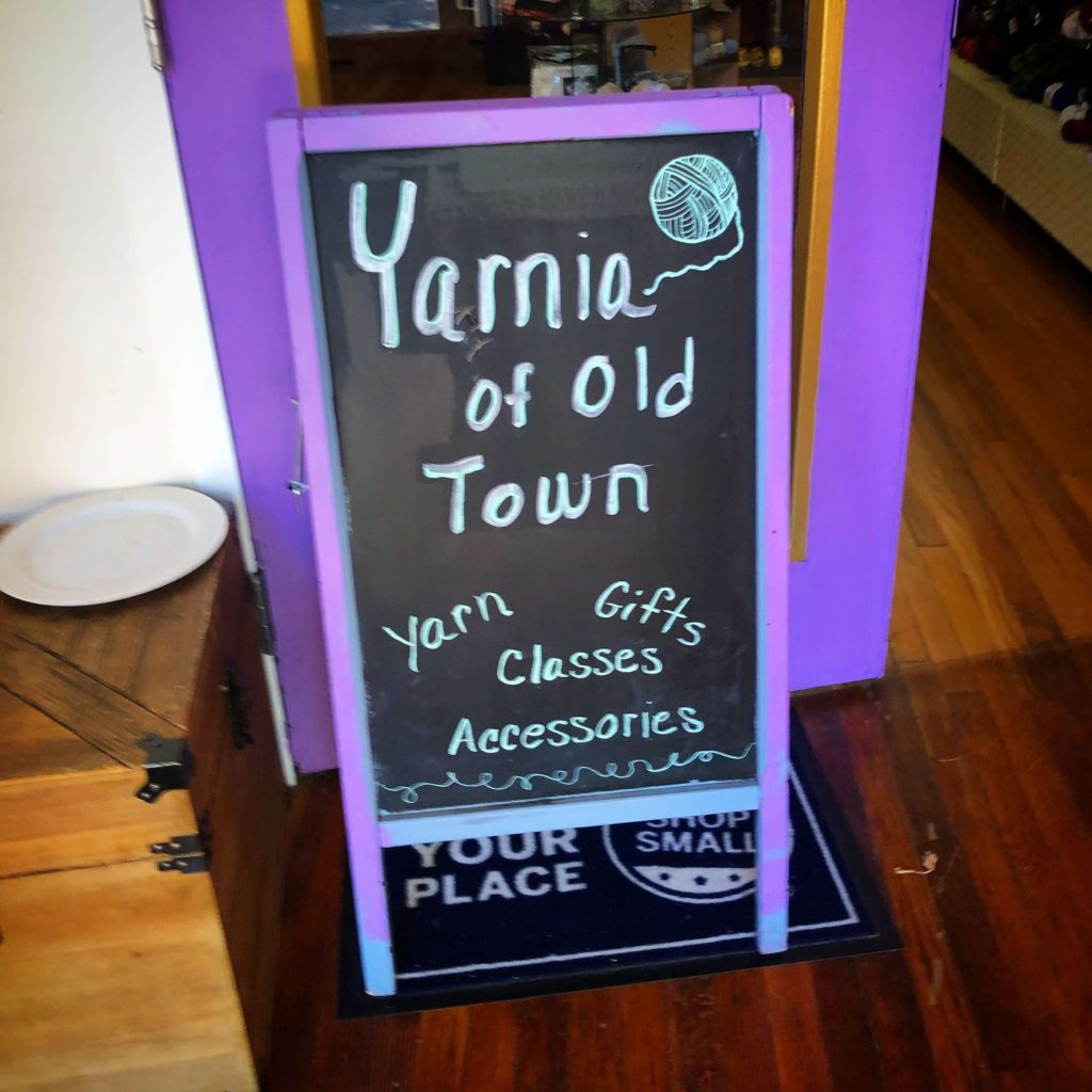 a chalk sandwich board reads "Yarnia of Old Town, yarn, gifts, classes, accessories"