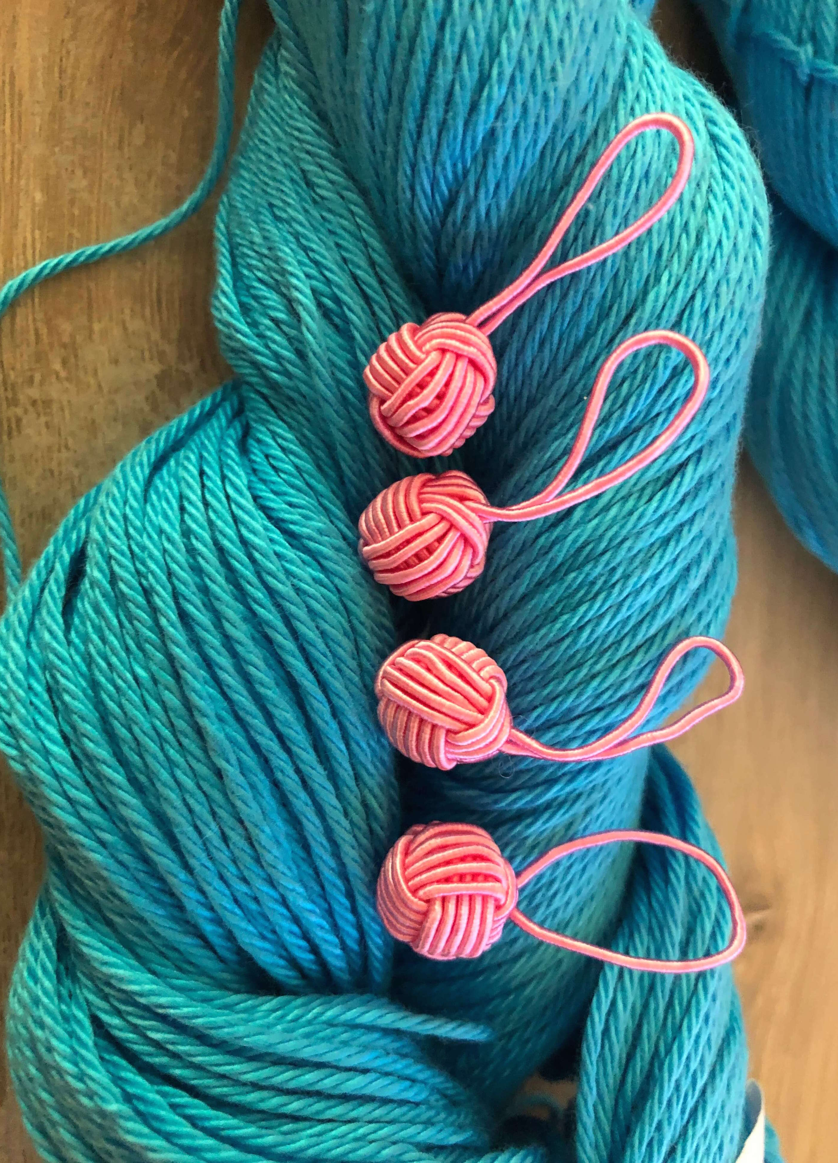 four yarn ball-shaped stitch markers lined up on a skein of yarn