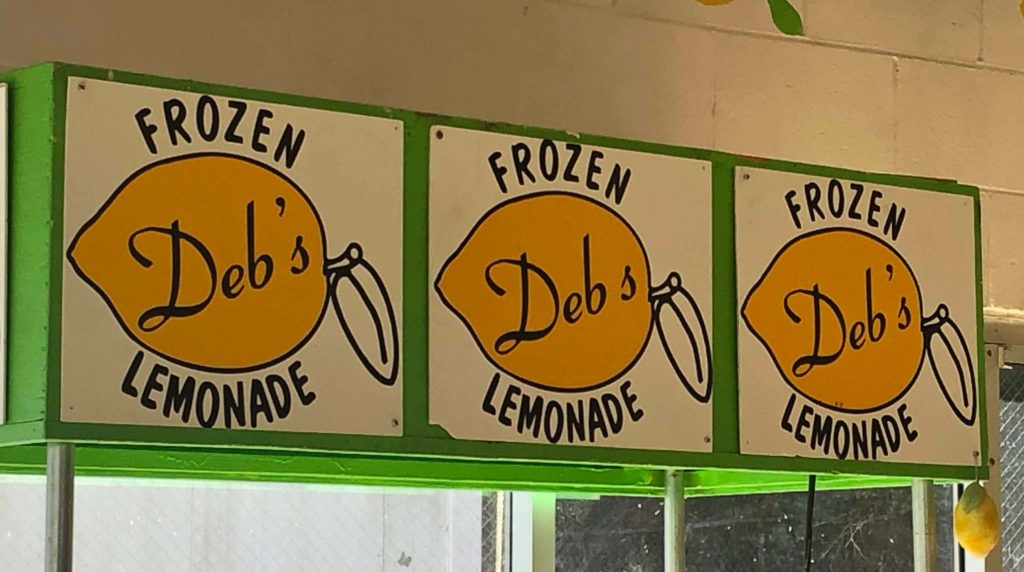 three identical signs feature large lemons and read "Deb's Frozen Lemonade"