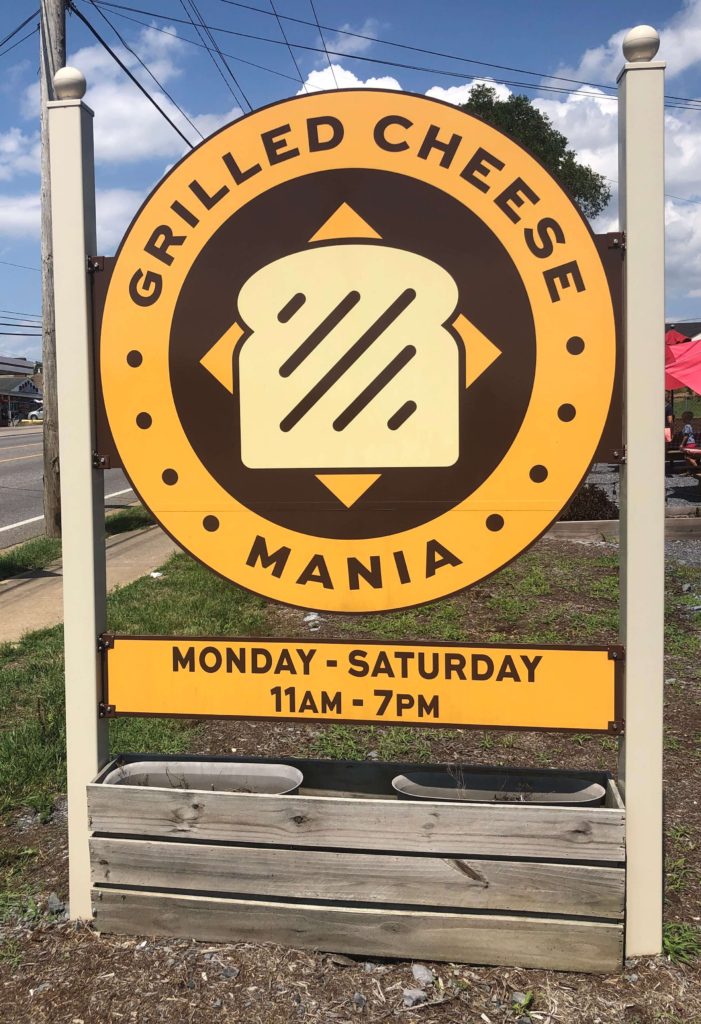 A large sign with a sandwich on it reads "Grilled Cheese Mania, Monday - Saturday, 11AM - 7PM"