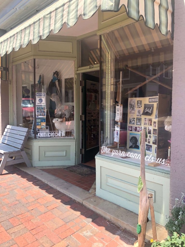 a storefront window reads "KNIT CROCHET the yarn connects us..."