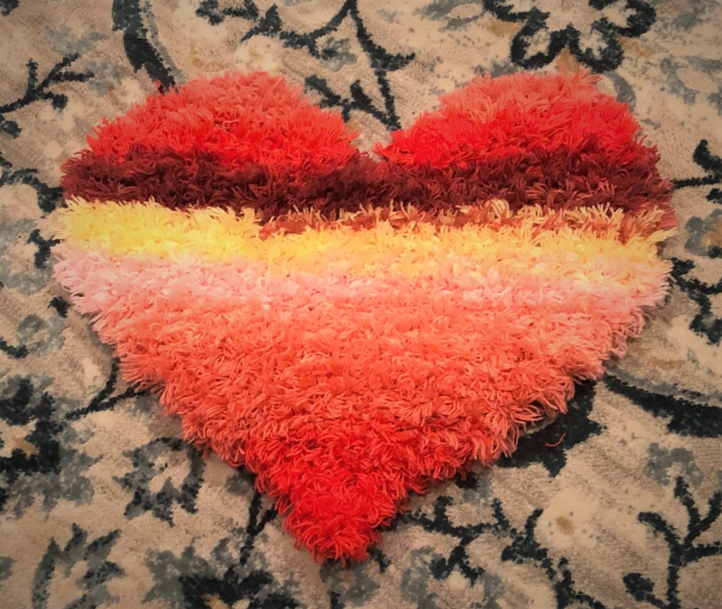 the Cordata Heart Rug, a shag, heart-shaped rug, on a carpet of contrasting color