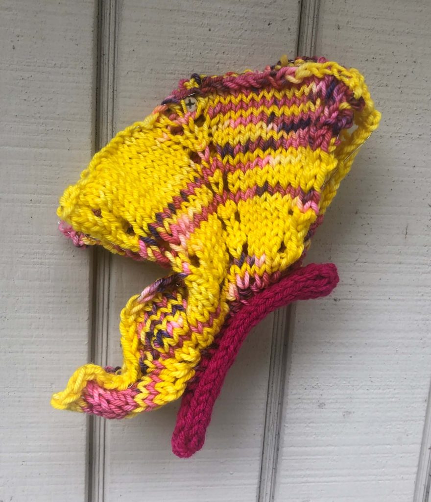 a knitted butterfly turned on its side, as if flying, and hanging on the wall