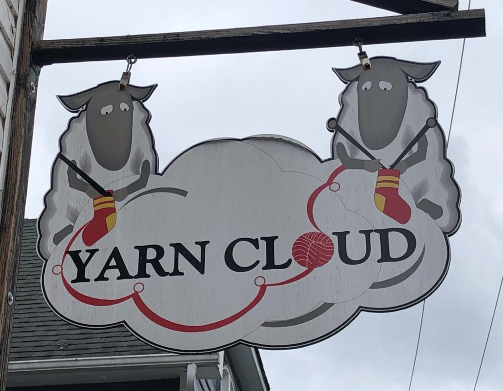 the Yarn Cloud sign features two sheep knitting socks