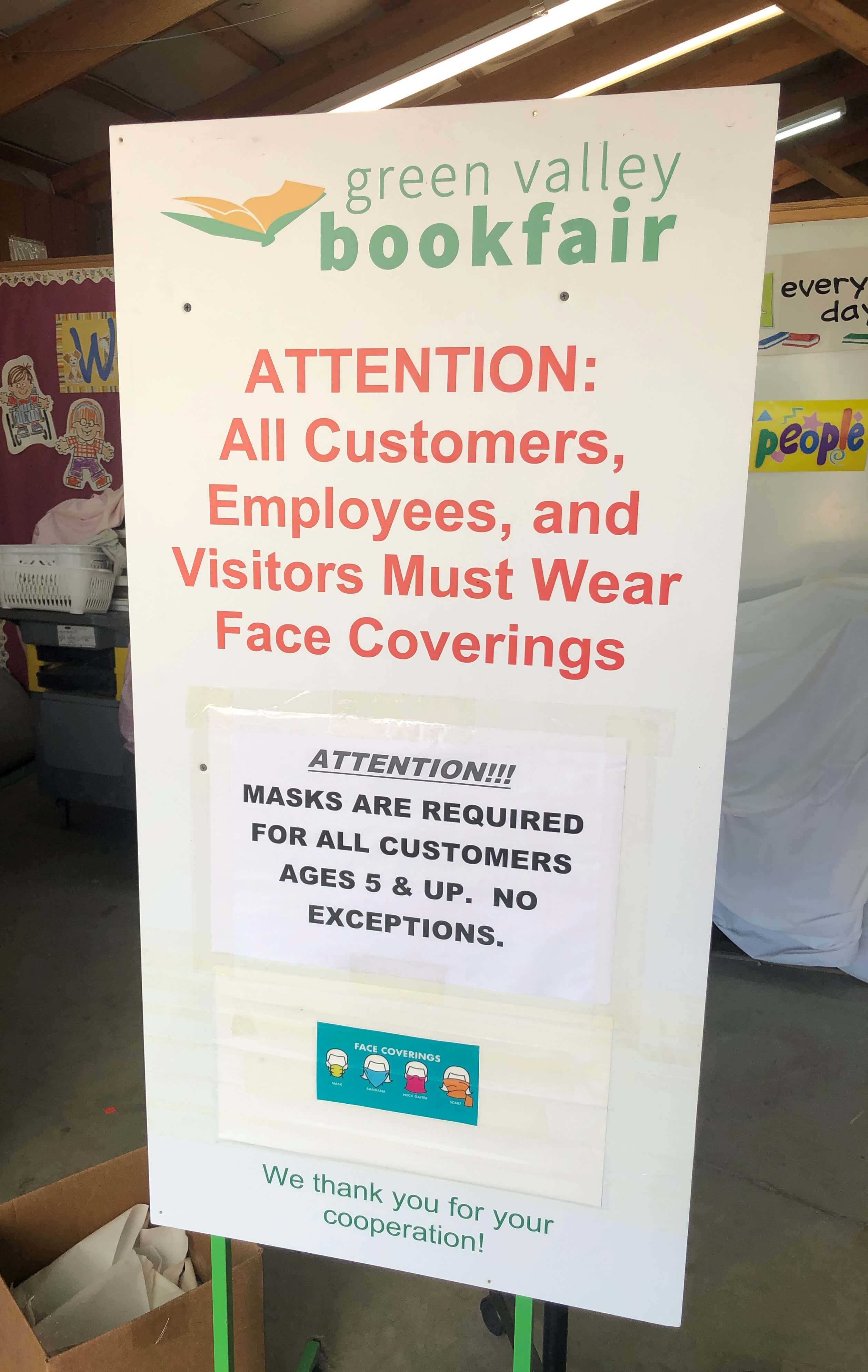 a sign that reads
"Green Valley Book Fair
Attention: All Customers, Employees, and Visitors Must Wear Face Coverings

Attention!!!
Masks are required for all customers ages 5 & up. No exceptions.

We thank you for your cooperation!"