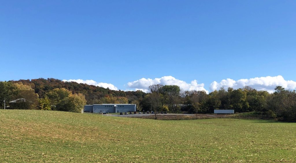 a large, open field lined with trees with a warehouse visible in the distance