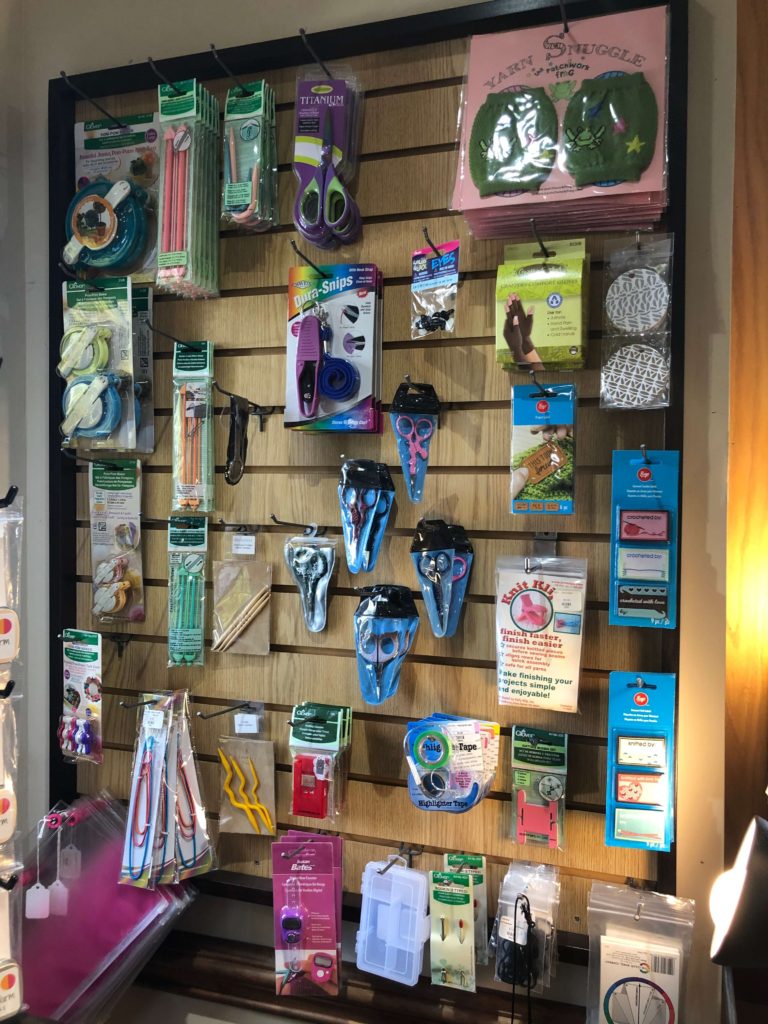 a rack displaying notions including scissors, yarn snuggles, pompom makers, and gift tags
