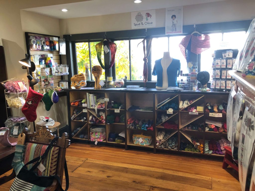 a yarn shop interior with shelves of yarn, racks of notions, and several sample pattern finished objects