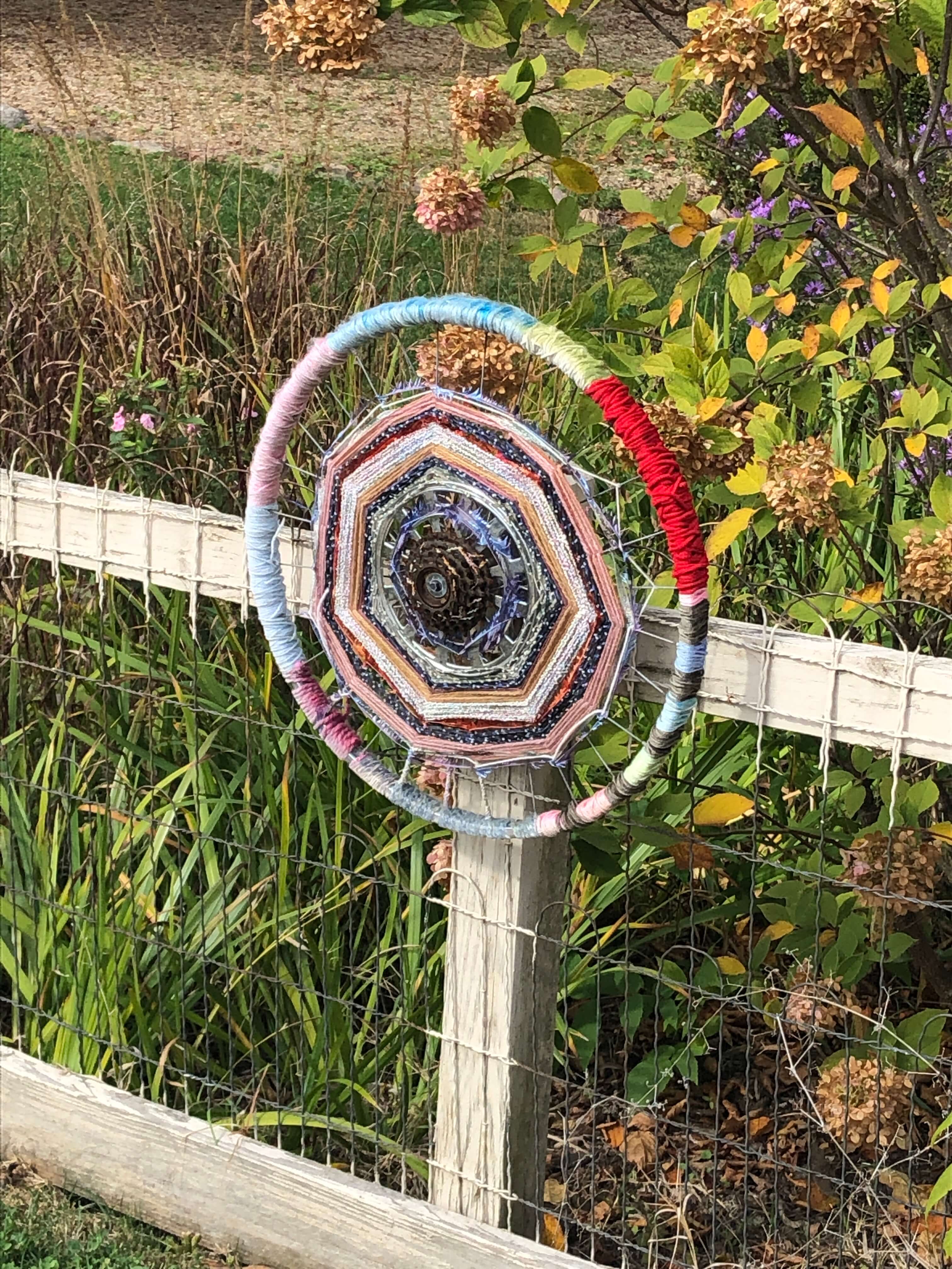 a yarn-bombed bicycle wheel attached to a fencepost