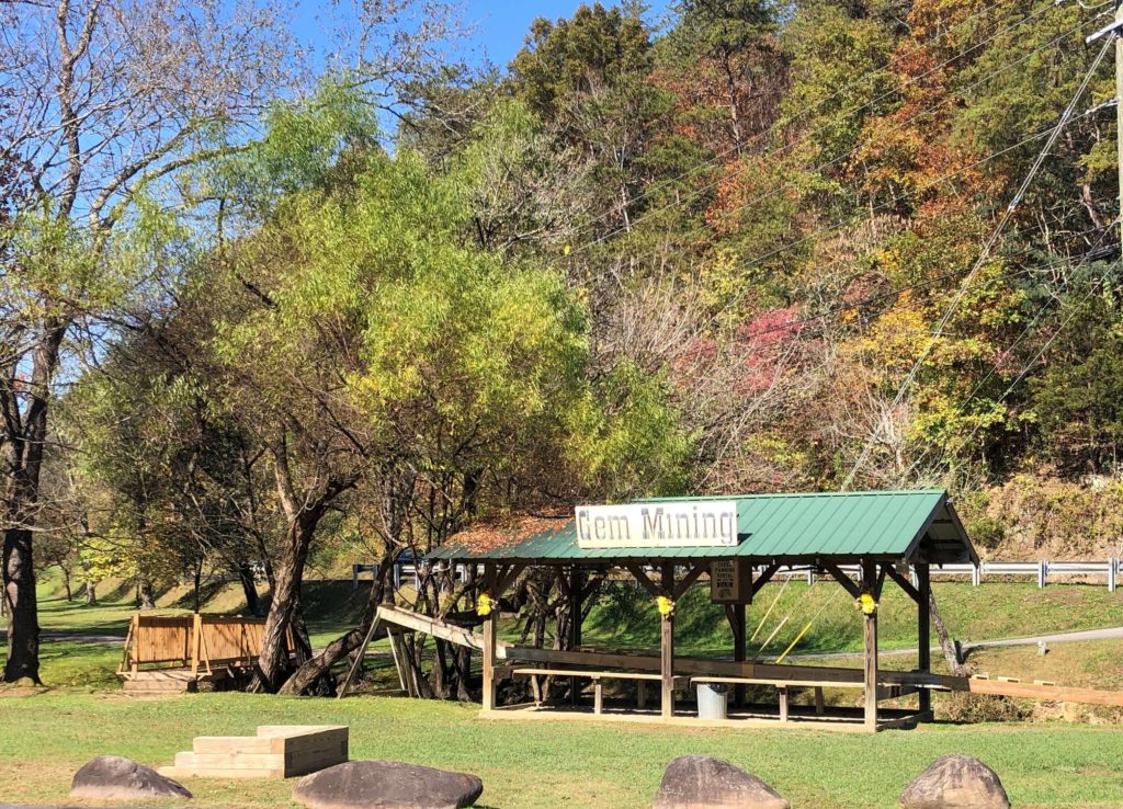 a shelter with a sign reading GEM MINING waits alongside a creek