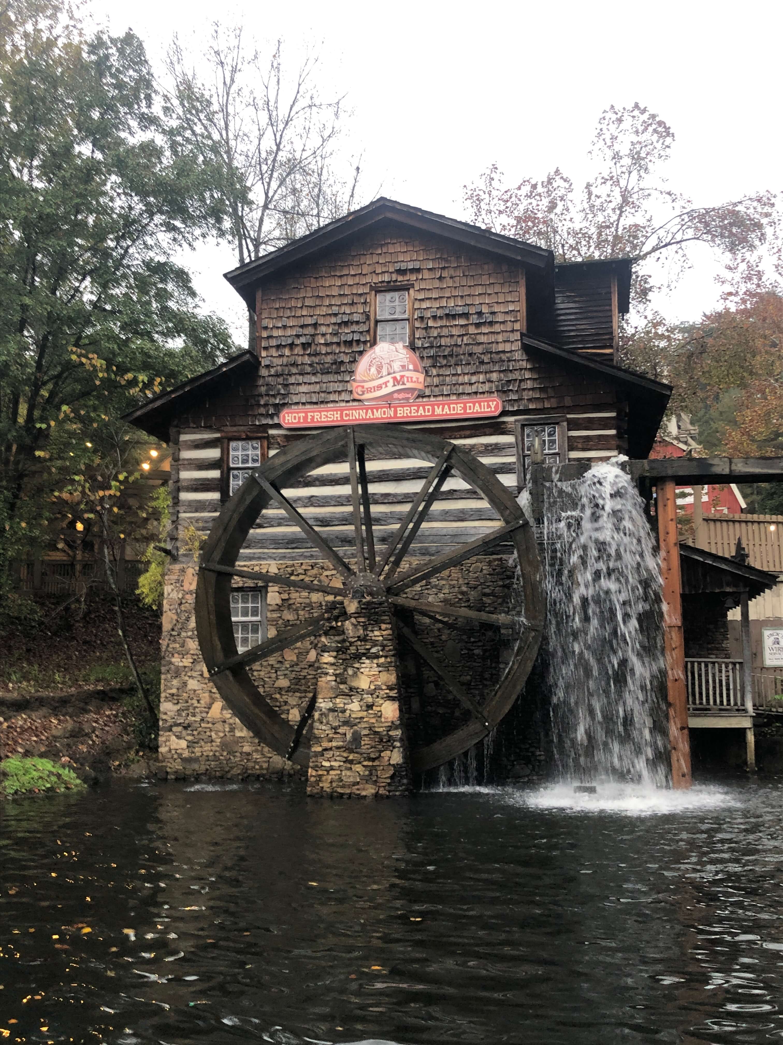 an exterior of the grist mill at Dollywood shows flowing water and a sign that reads HOT FRESH CINNAMON BREAD MADE DAILY