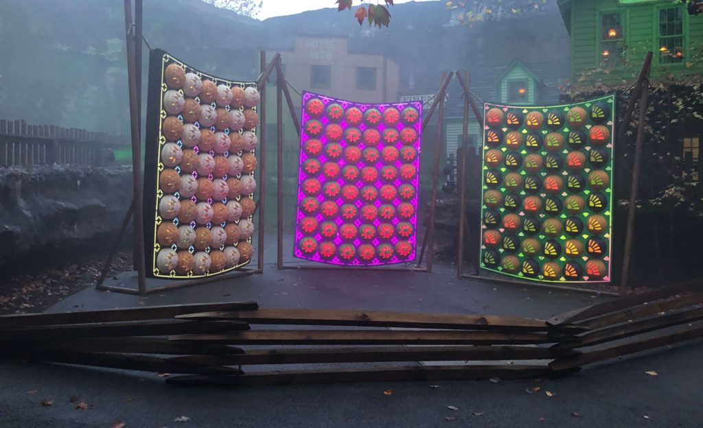 three pumpkin quilts with color-changing lights are displayed behind a Civil War-era fence