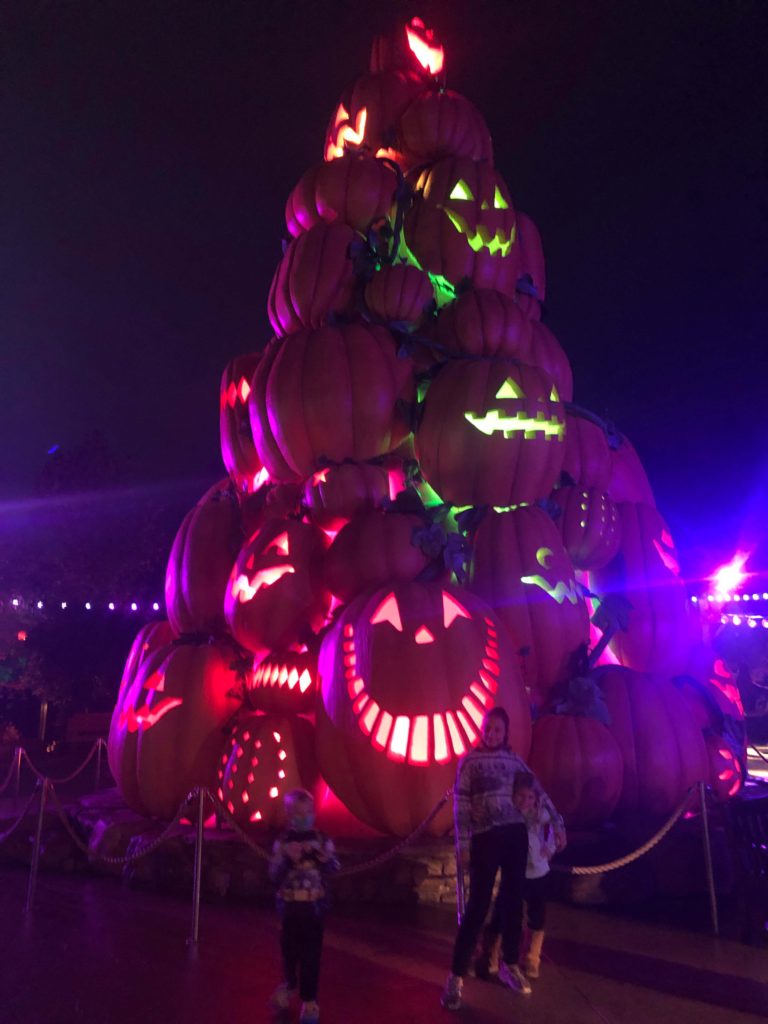 three children pose in front of a forty-foot tower of smiling jack-o-lanterns