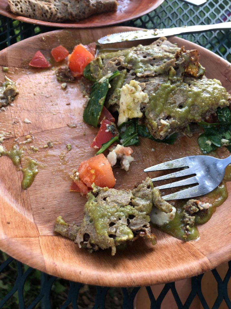 a half-eaten pesto crepe with tomatoes, coconut cheese, greens, and pesto sauce