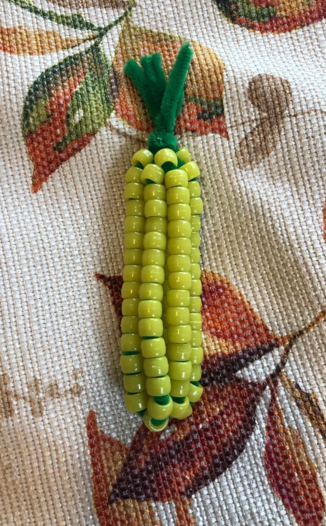 a corn cob craft made of pony beads and chenille stems on an autumn tablecloth