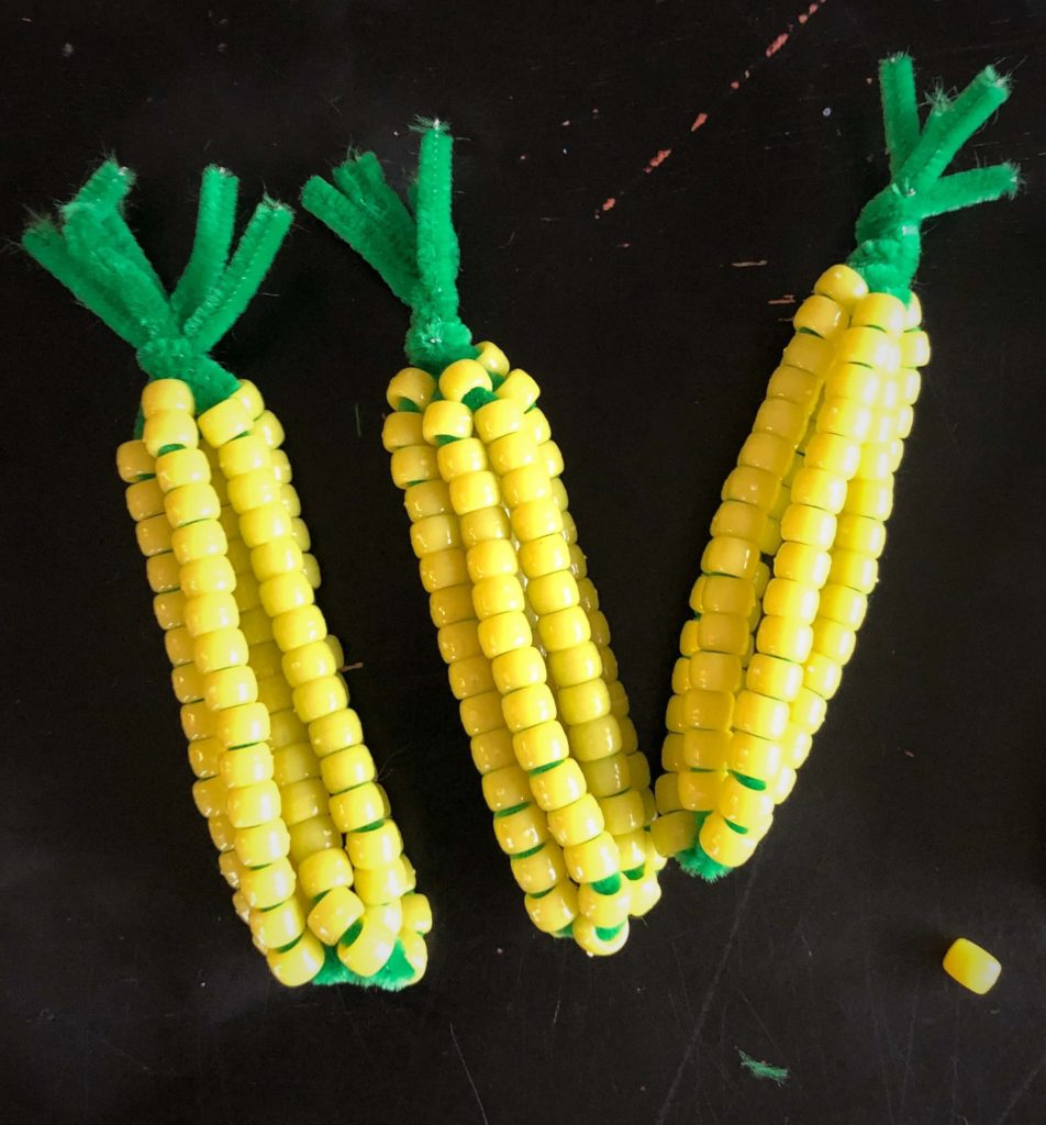 three finished corn cob crafts made of beads and a stray kernel (bead)