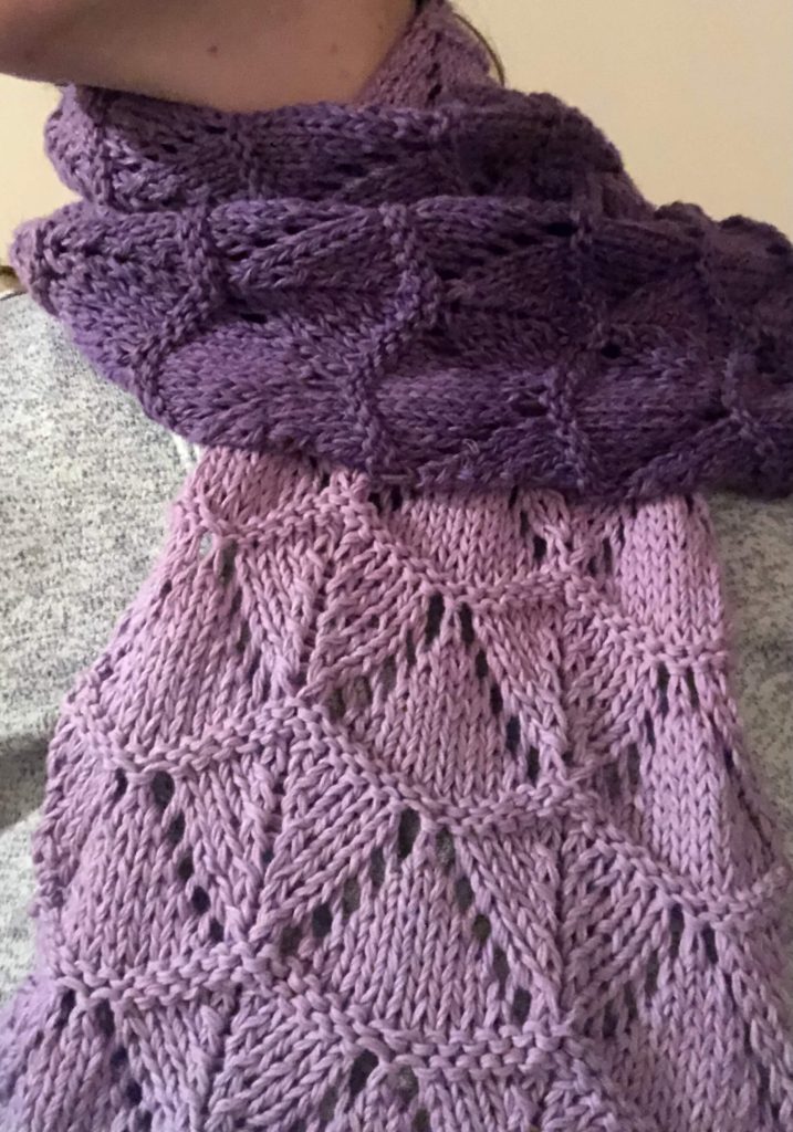 a scarf around a woman's neck worked in a textured pattern in a yarn that gradually changes color
