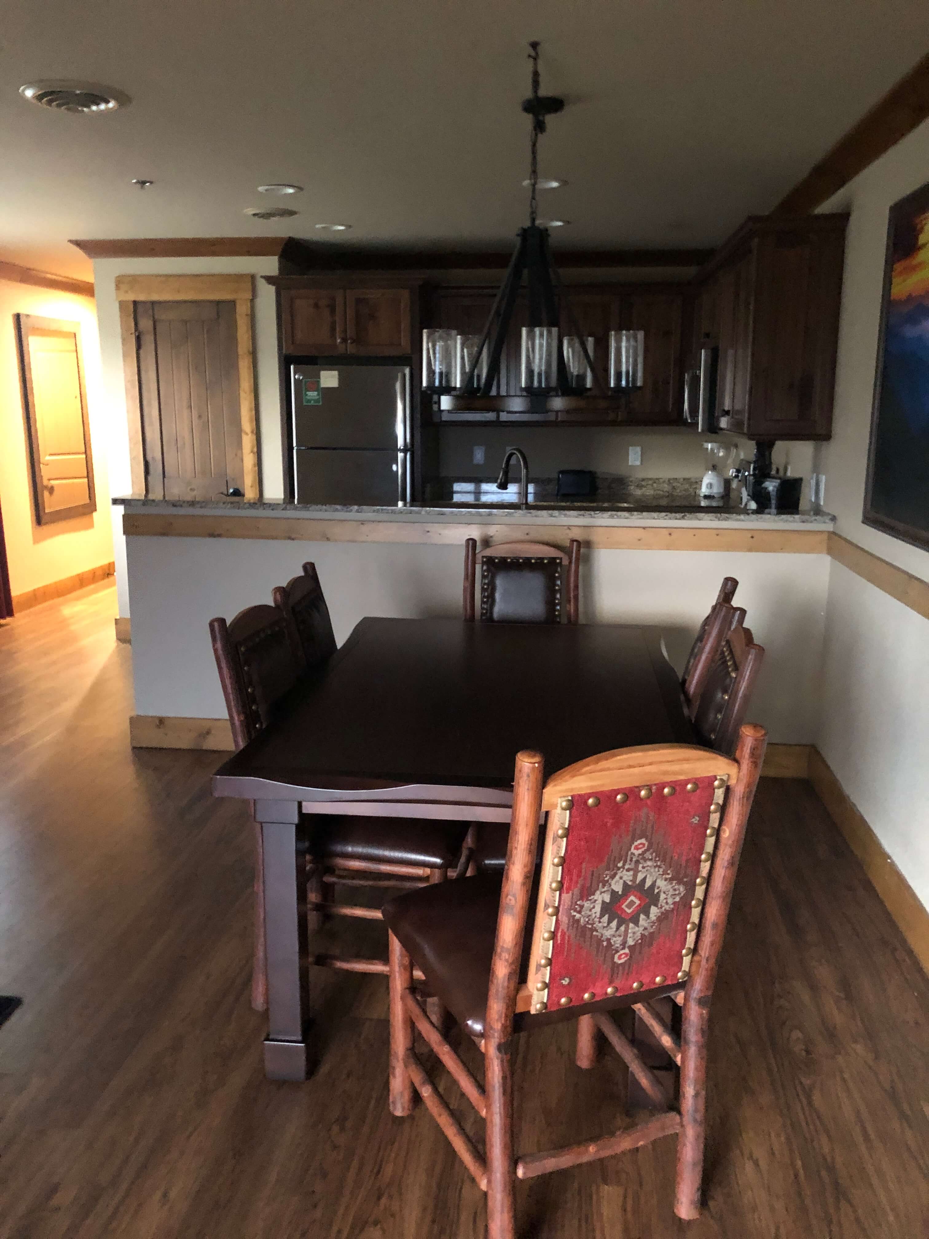 a dining table with six chairs beside a half-wall separating it from a large kitchen