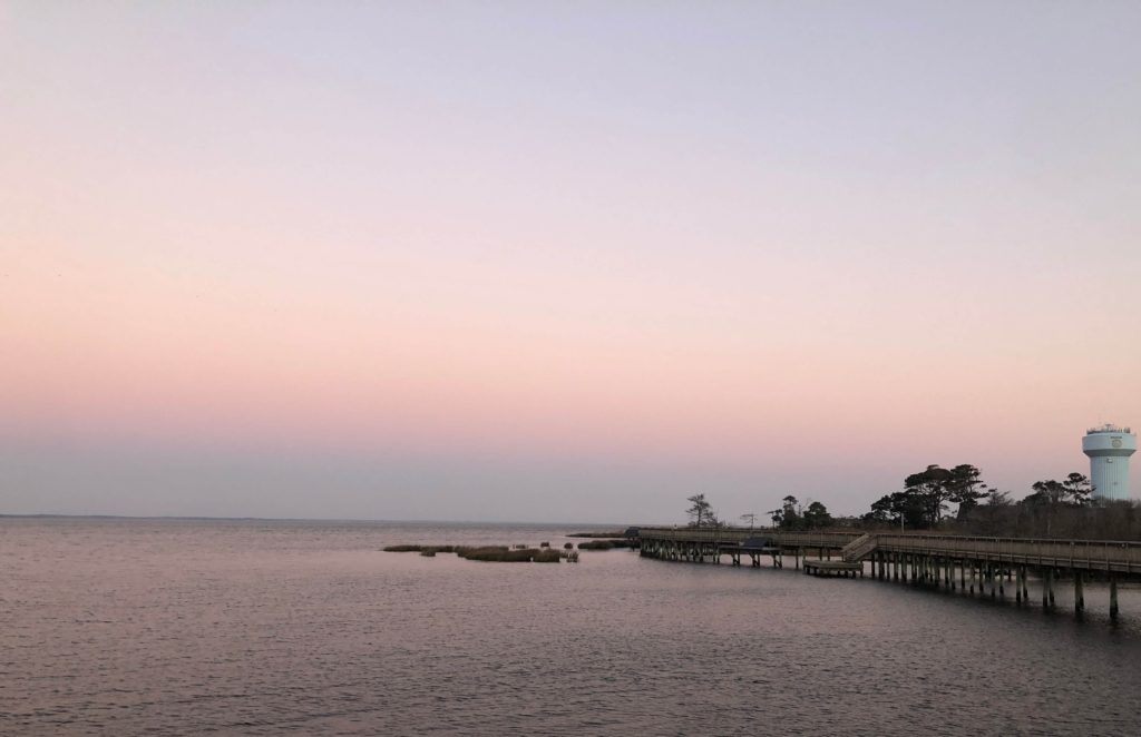 a view of the Currituck sound at sunrise with the Duck boardwalk and Duck water tower just visible in the distance
