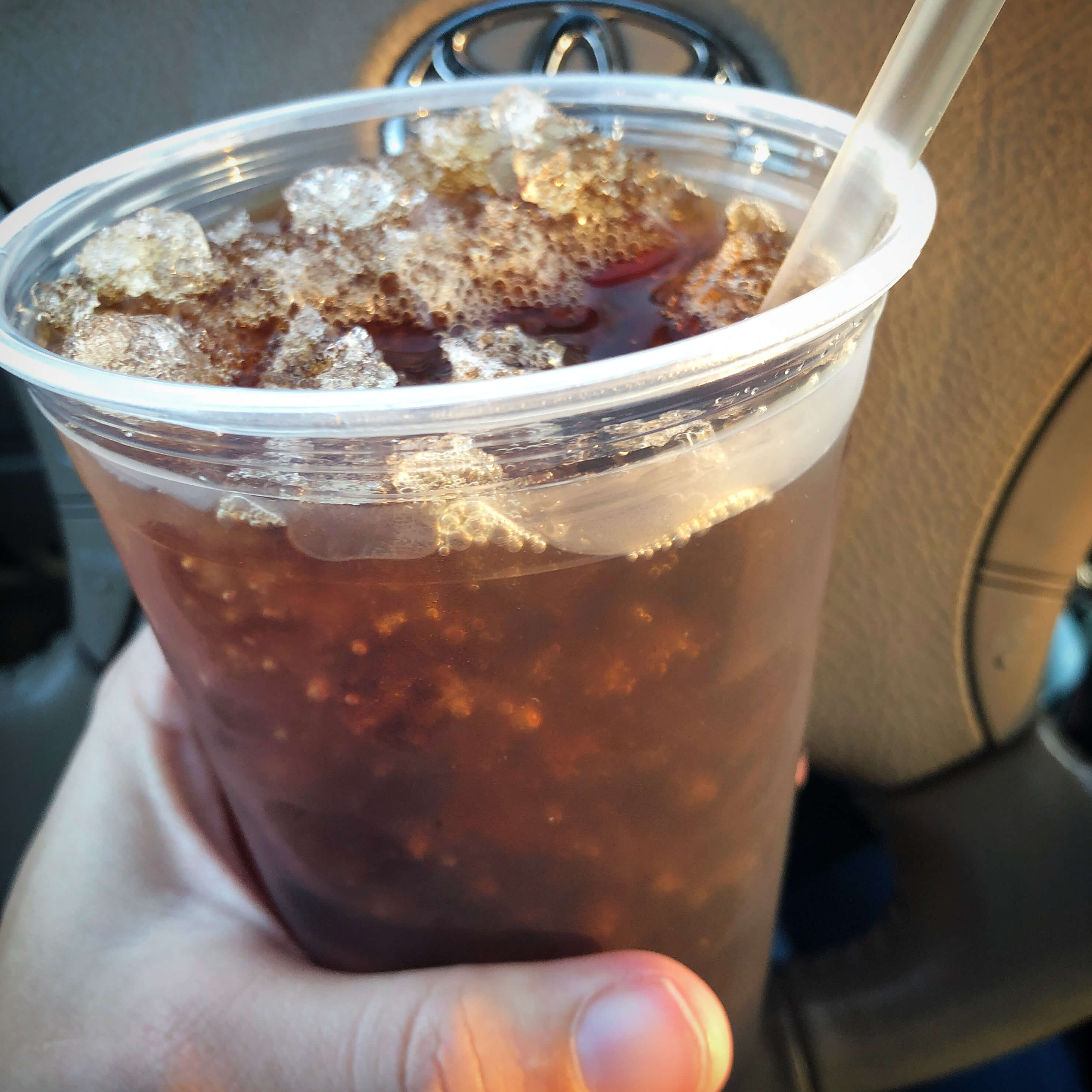 a hand holds a large iced coffee (black) with a straw and crushed ice