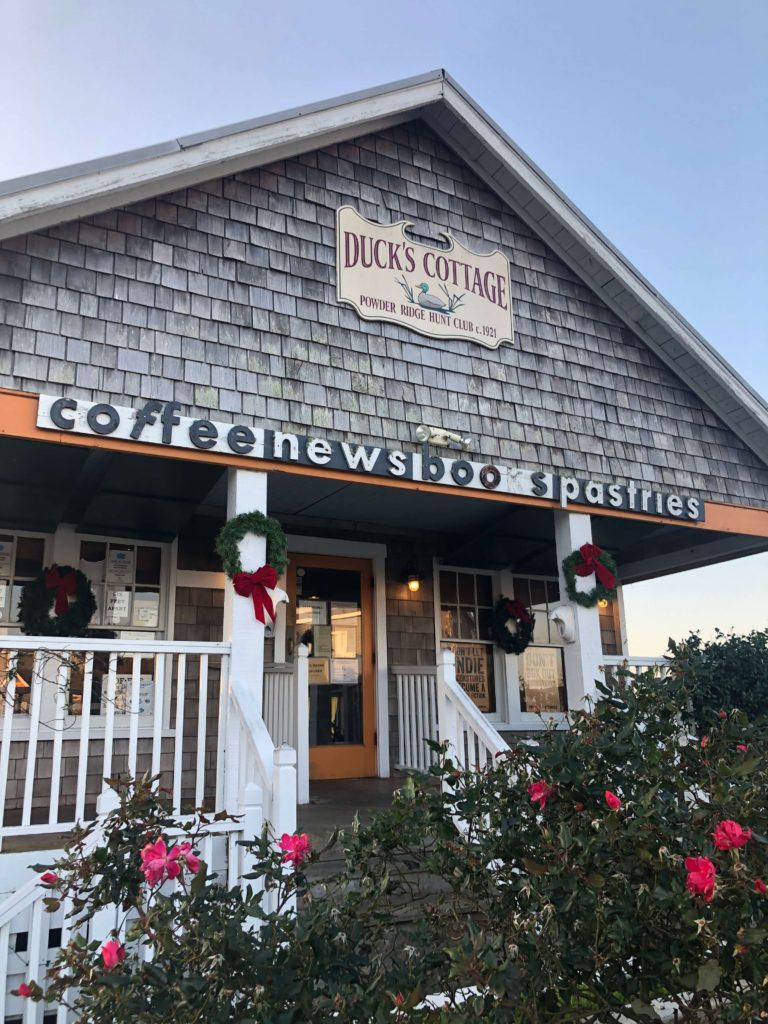 a small cottage with wooden shingles bears a sign that reads: Duck's Cottage, coffee, news, books, pastries