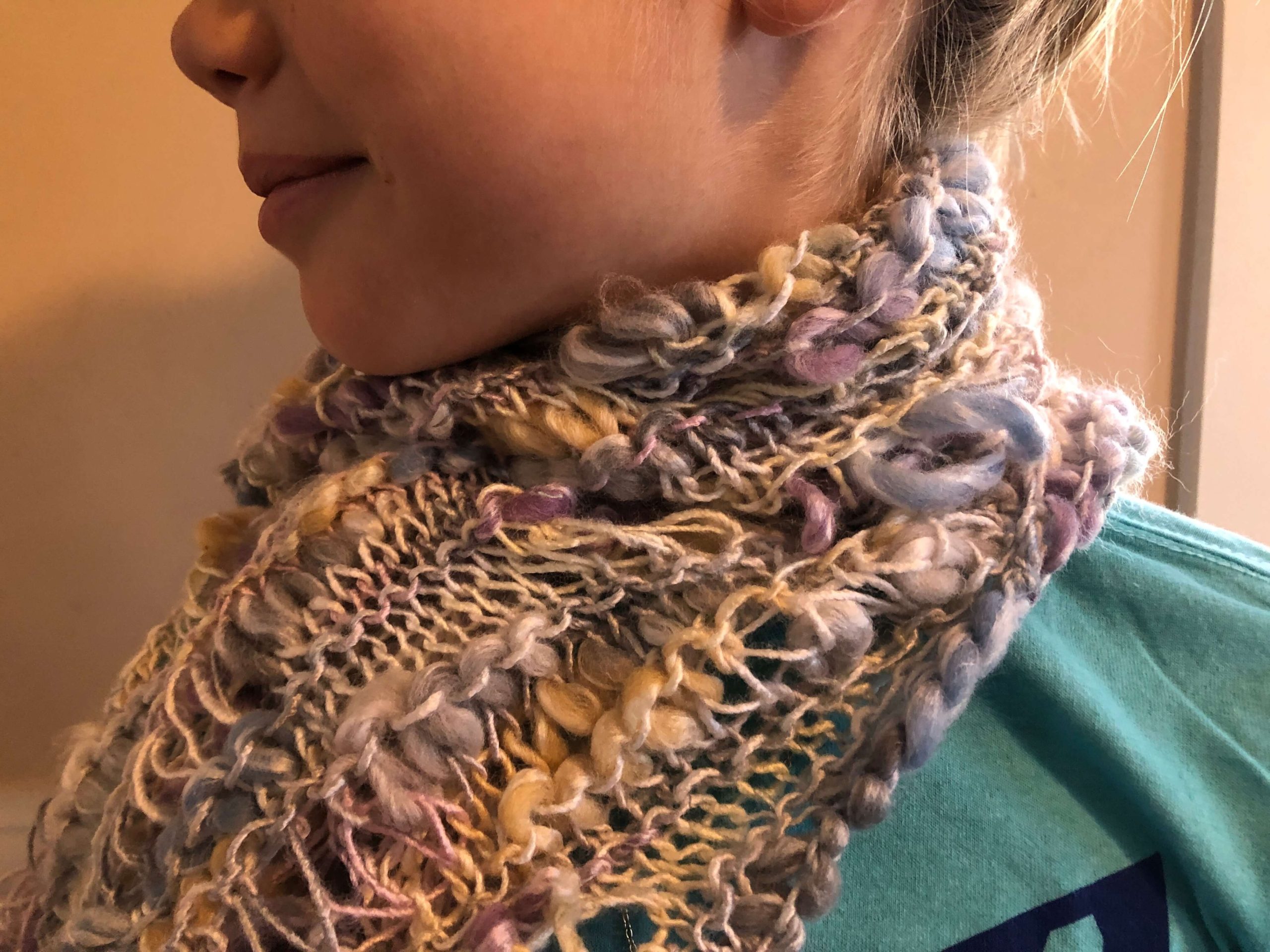 a child wears the Fairy Lights Cowl, a dropped stitch cowl knit in yarn of varying textures