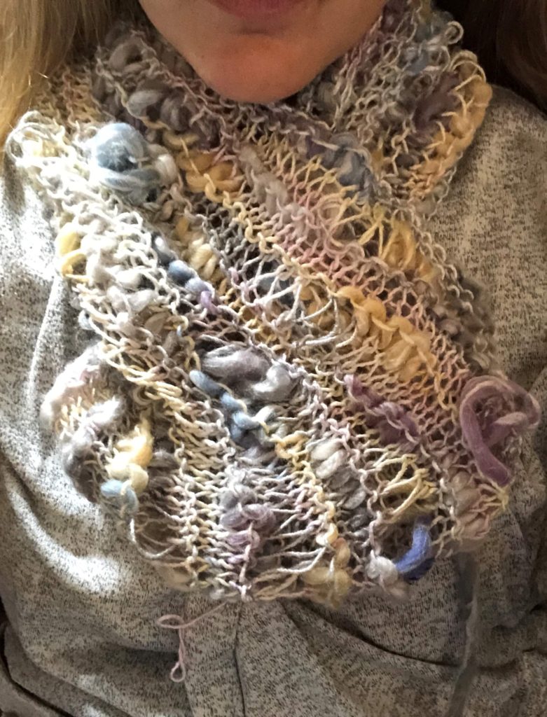 a woman wears the Fairy Lights Cowl, a dropped stitch cowl knit in yarn of varying textures