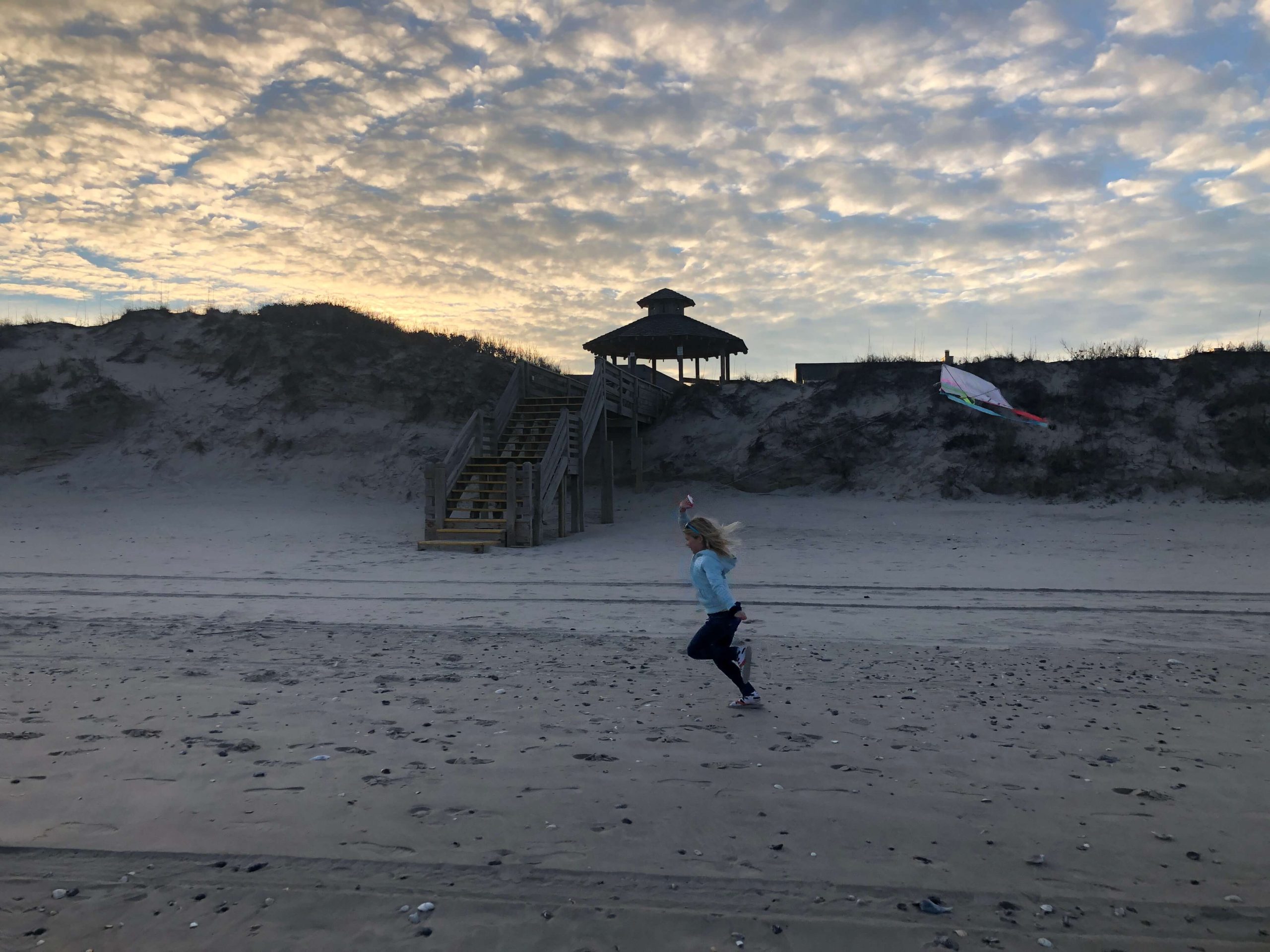 a young girl runs across the beach pulling a kite