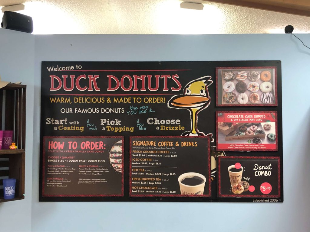 a large sign features menu at Duck Donuts plus instructions on ordering