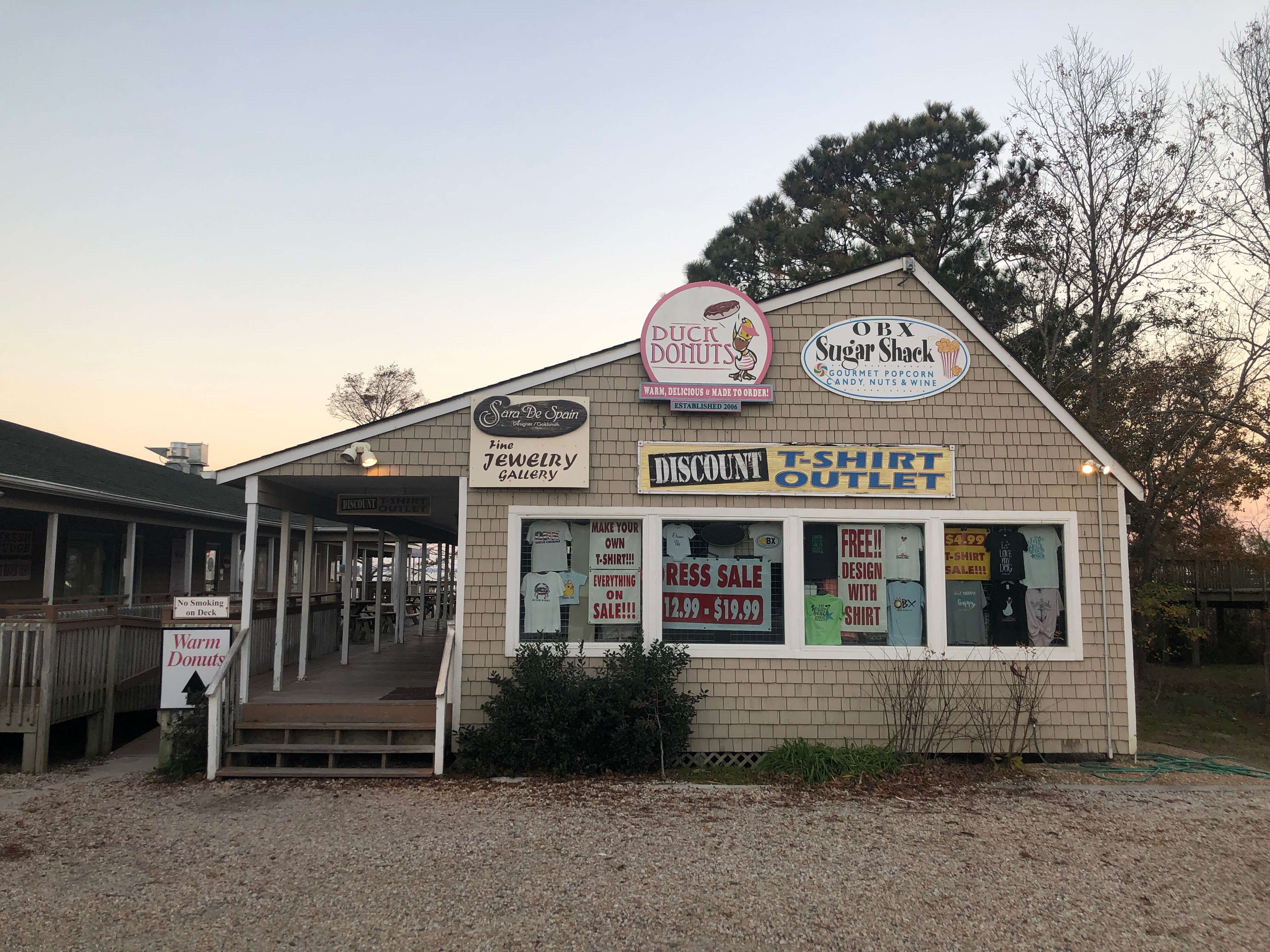 the exterior of a shingled shop building featuring signage for Duck Donuts and other OBX shops
