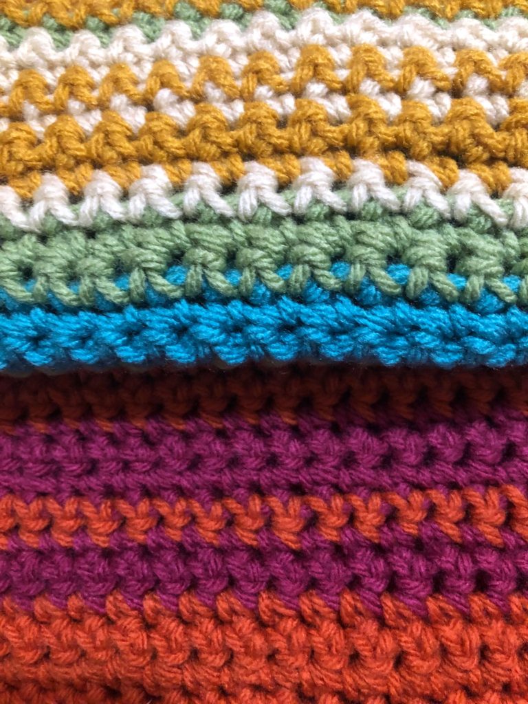 a close-up of a crocheted temperature blanket with cool colors reflecting colder weather and warm colors reflecting hotter weather
