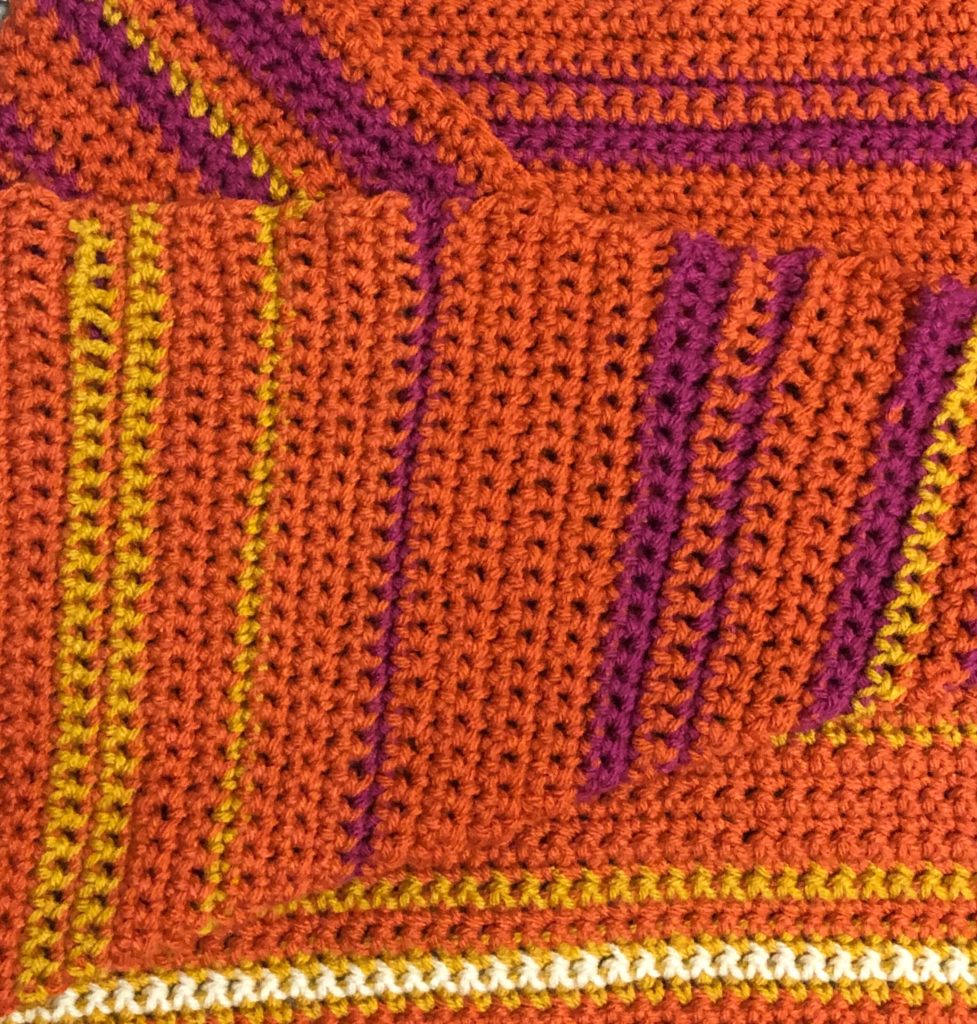 a crocheted temperature blanket in warm colors representing summer months, crocheting by a knitter