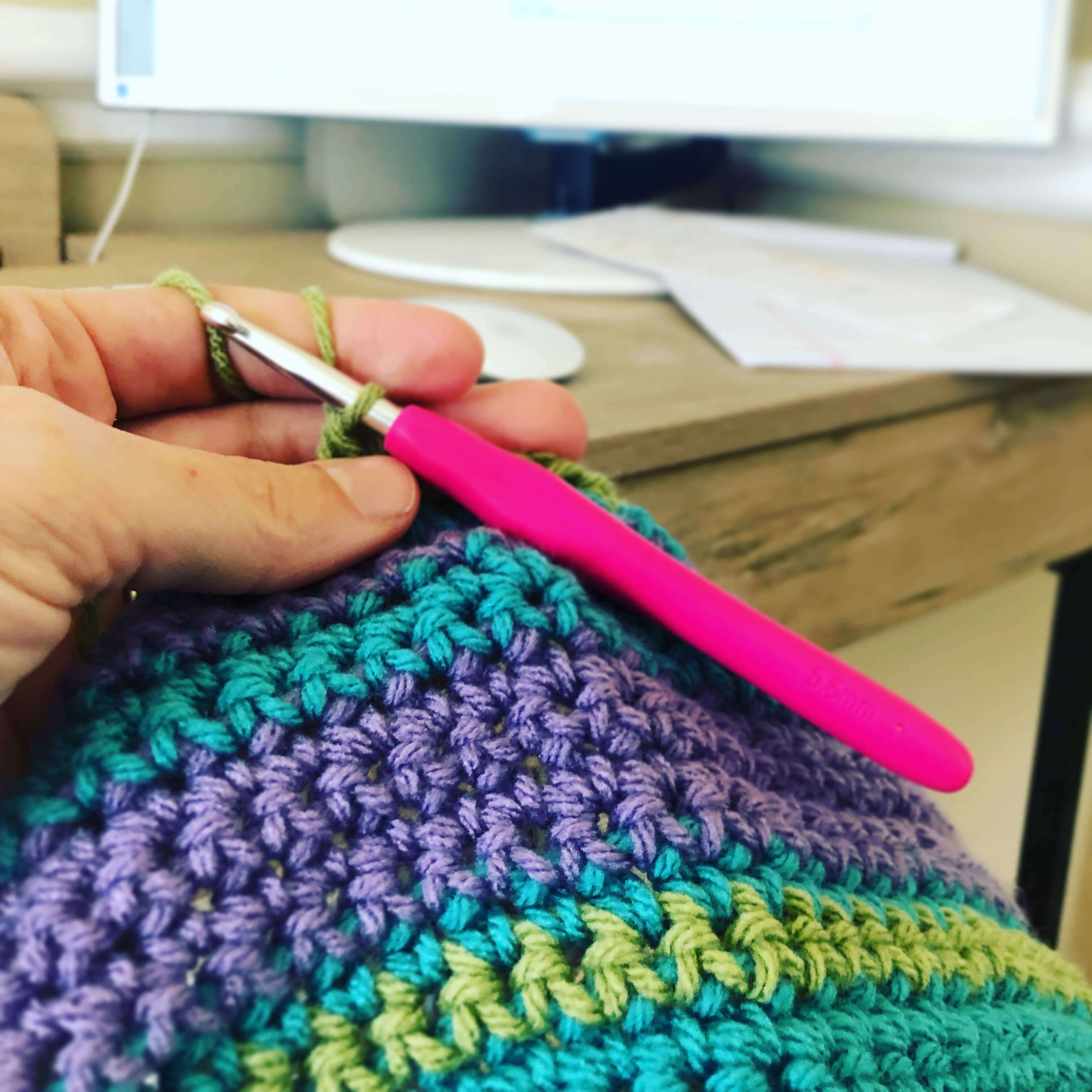 a knitter holding a crochet hook in position for the next stitch of an afghan