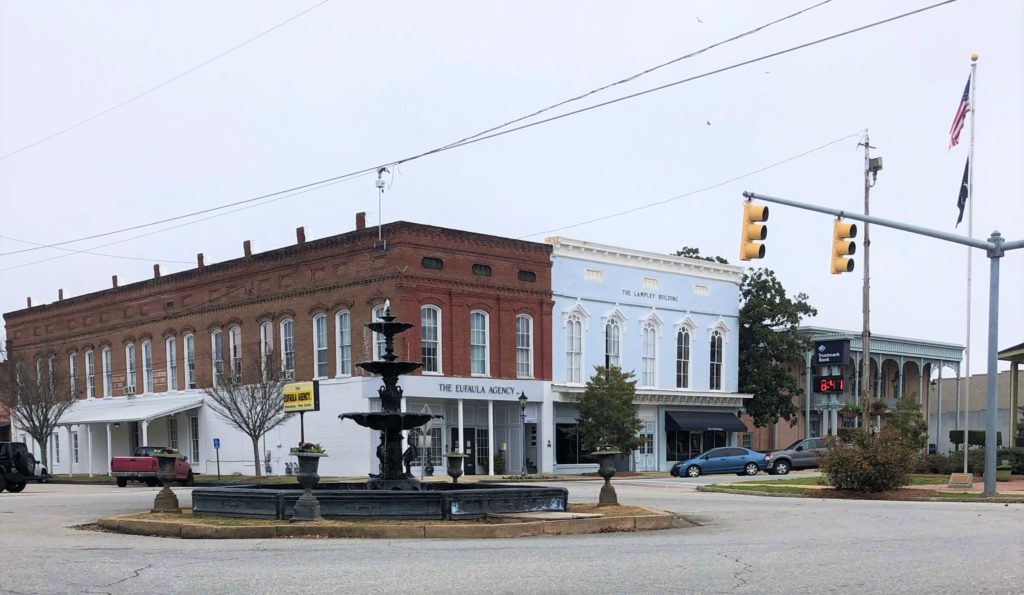 the streets of downtown Eufaula, Alabama: historical storefronts, flags flying high, and an elaborate center-street fountain
