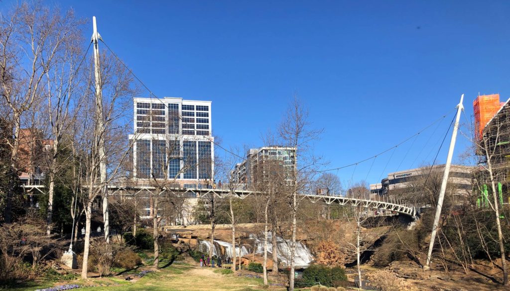 a suspension bridge stretches over a river in downtown Greenville