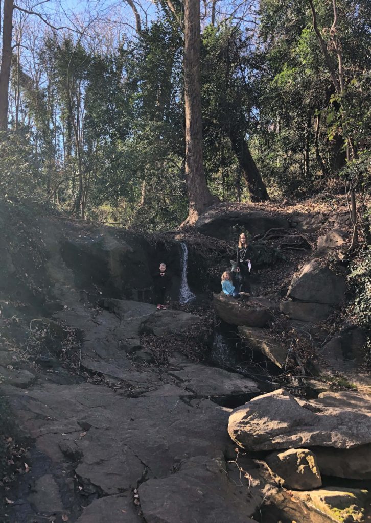 three children pose by a spring with a small waterfall