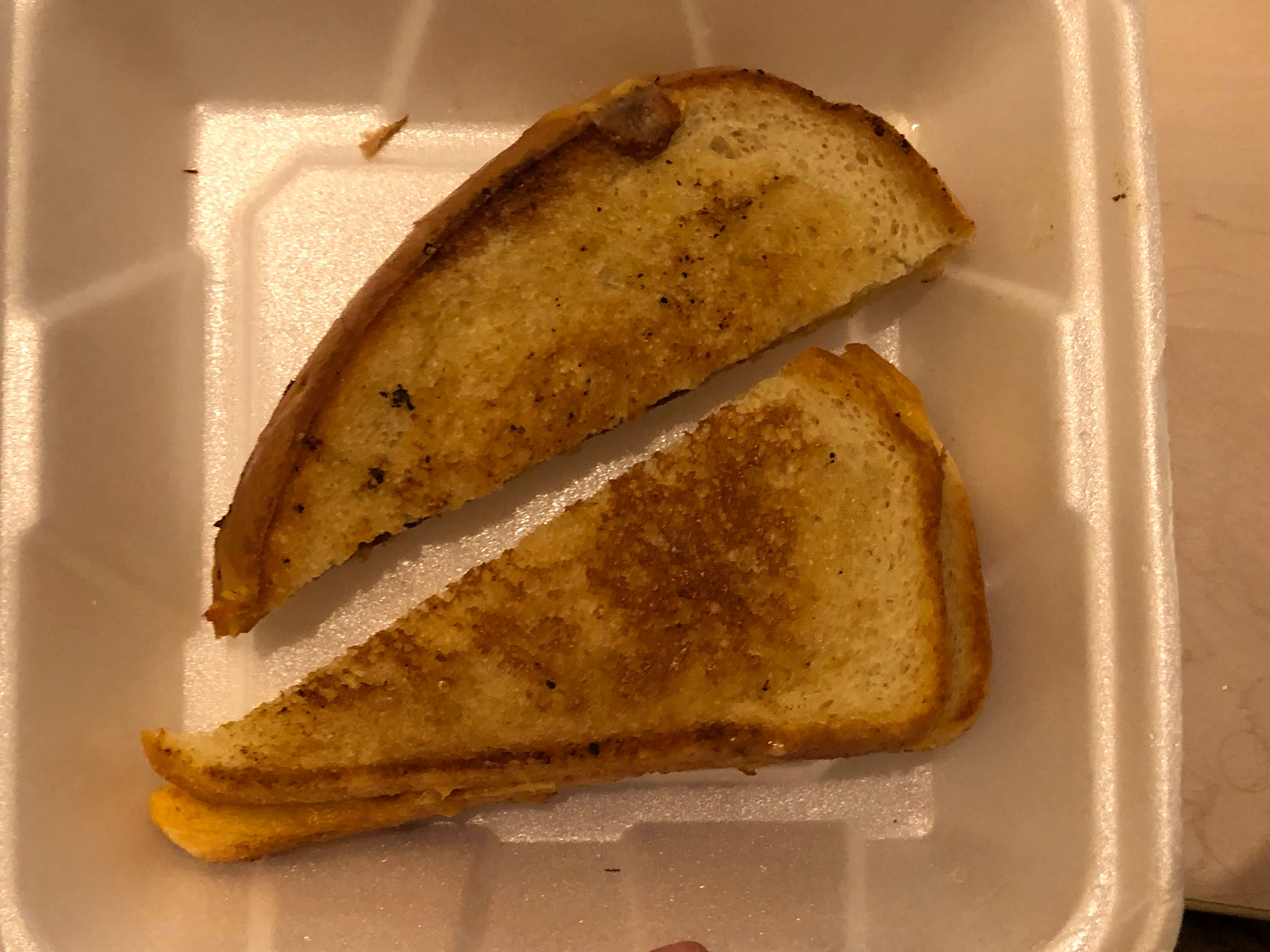 a grilled cheese sandwich, cut diagonally, in a Styrofoam clamshell
