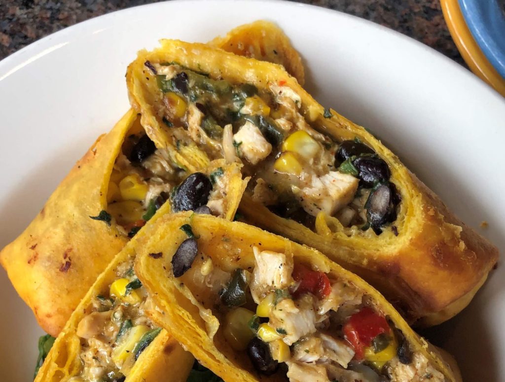 egg rolls sliced diagonally revealing a filling of chicken, cheese, black beans, corn, onions, and tomatoes
