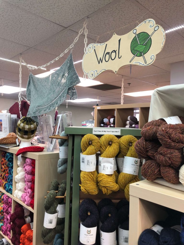 hanks of yarn line the shelves under a sign that reads "Wool"