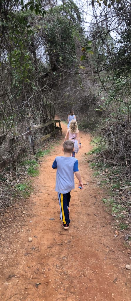 three children hiking down a trail of red dirt with vines hanging overhead